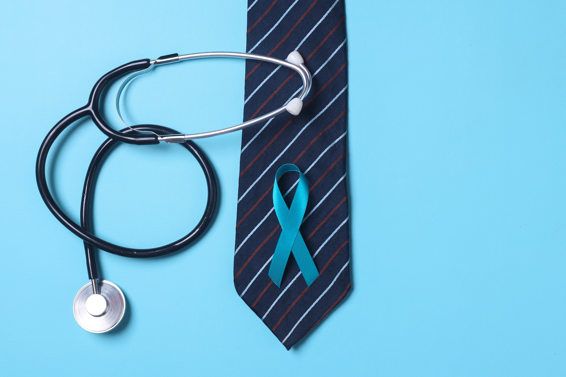 Stethoscope, striped tie and prostate cancer awareness ribbon against blue background